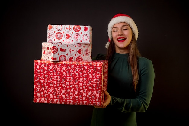 Beauty happy female with Christmas hat and gifts on black background