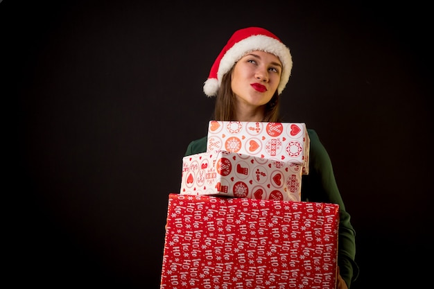 Beauty happy female with Christmas hat and gifts on black background