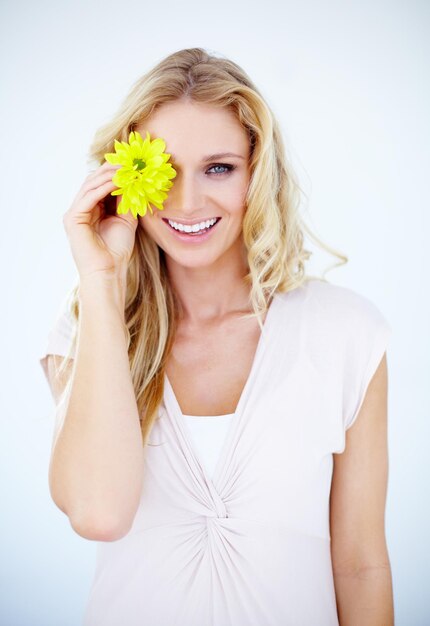 Foto bellezza felice e ritratto di una donna con un fiore in uno studio con una routine cosmetica naturale e viso trucco sorriso e modello femminile con una pianta floreale gialla isolata da uno sfondo bianco