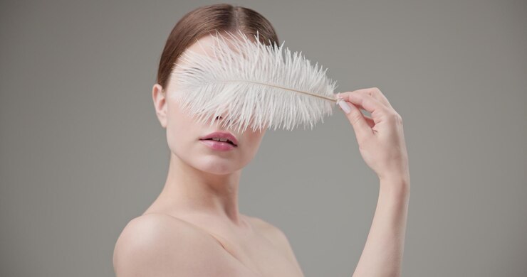 Beauty health cosmetics antiaging therapy and skin care concept young beautiful brunette Caucasian woman holding a white fluffy feather in her hands tenderness lightness and softness