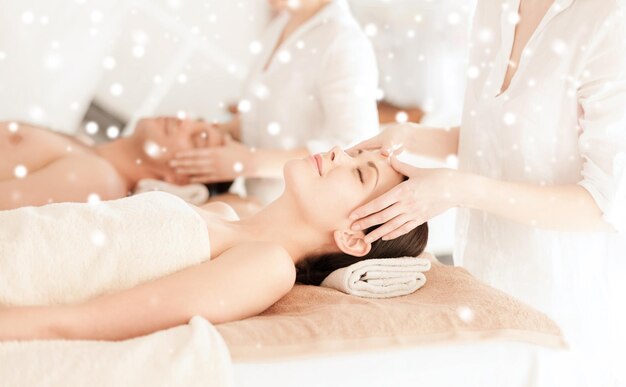 beauty, health, holidays, people and spa concept - happy couple with closed eyes getting facial massage lying in spa salon