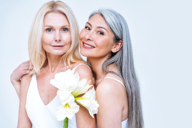 beauty image of two women with different age, skin and body posing in studio for a body positive photoshooting. Mixed female models in lingerie on colored backgrounds