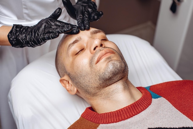 Foto un impiegato dell'industria della bellezza distribuisce olio idratante sul viso di un ragazzo con le mani