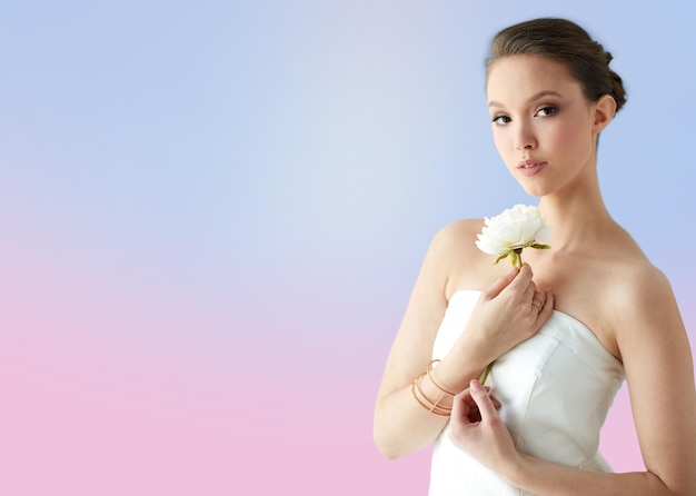 beauty, jewelry, people and luxury concept - beautiful asian woman or bride in white dress with peony flower, golden ring and bracelet over rose quartz and serenity gradient background