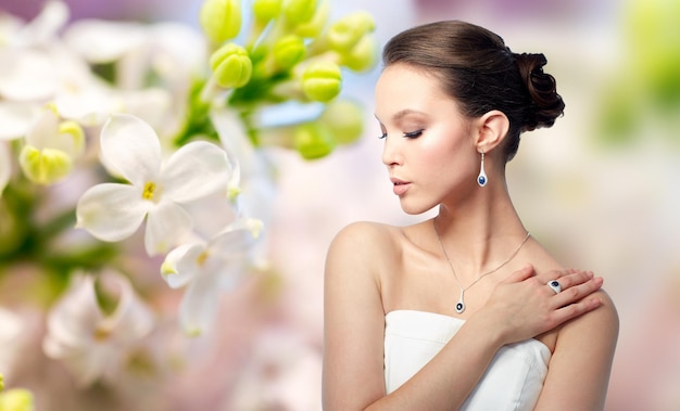 beauty, jewelry, people and luxury concept - beautiful asian woman or bride with earring, finger ring and pendant over natural spring lilac blossom background