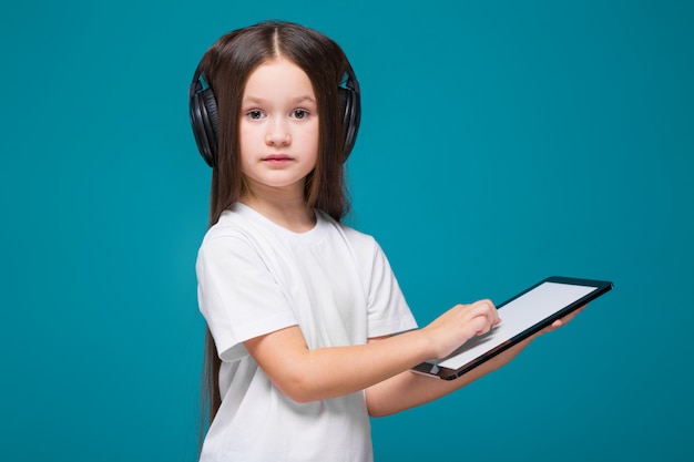 Beauty little girl in tee shirt and earphones with long hair, with tablet in hands