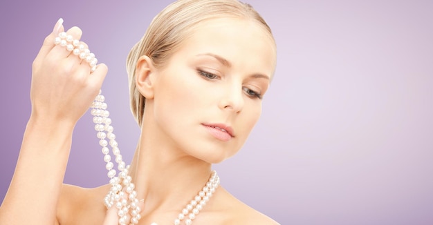 Photo beauty, luxury, people, advertisement and jewelry concept - beautiful woman with sea pearl necklace or beads in hand over violet background