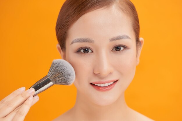 Beauty. Makeup. Beautiful woman applying dry cosmetic tonal foundation on the face using makeup brush.