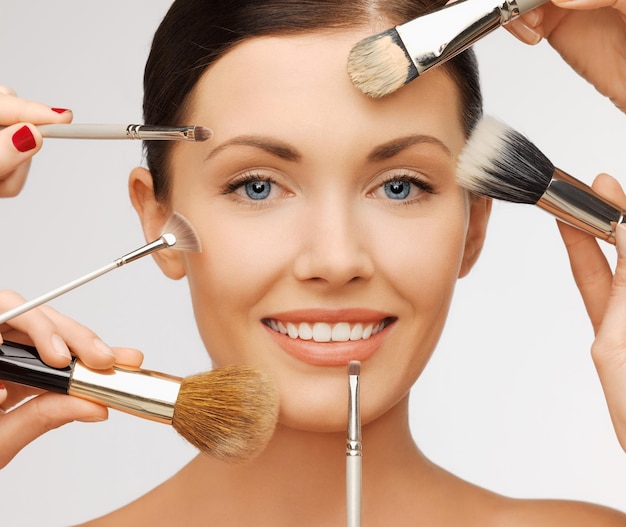 beauty and makeup concept - closeup portrait of beautiful woman getting professional make-up with many brushes