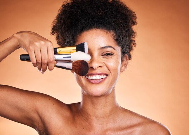 Beauty makeup and portrait of black woman with brushes in studio isolated on an orange background self care skincare and female model with cosmetics products or makeup brushes for skin aesthetic