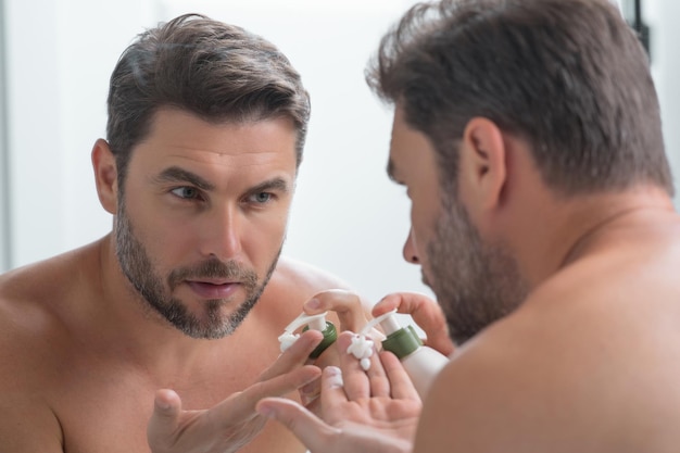 Beauty man applying cream on skin face handsome serious man enjoy fresh perfect skin applying facial