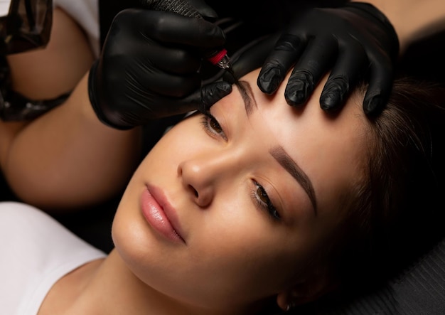 Photo beauty master making permanent tattoo with a machine