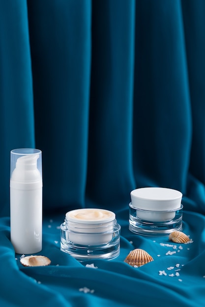 Beauty mineral moisturizer cream, shells, sea ââsalt  in glass jar, blue draped cloth.