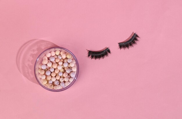 Beauty minimal layout Balls of powder and false eyelashes on pink background