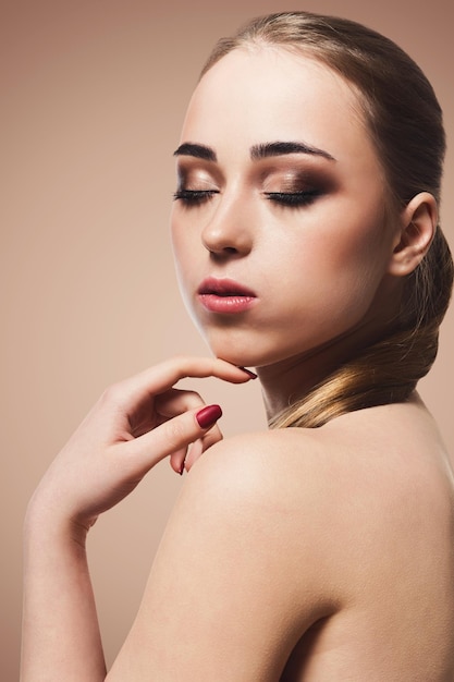 Beauty model on beige background, fashion shooting. Woman with makeup, perfect skin and hair posing to camera at studio, copy space