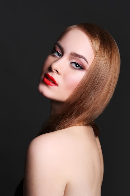 Beauty model on black background, fashion shooting. Woman with makeup, perfect skin and hair posing to camera at studio