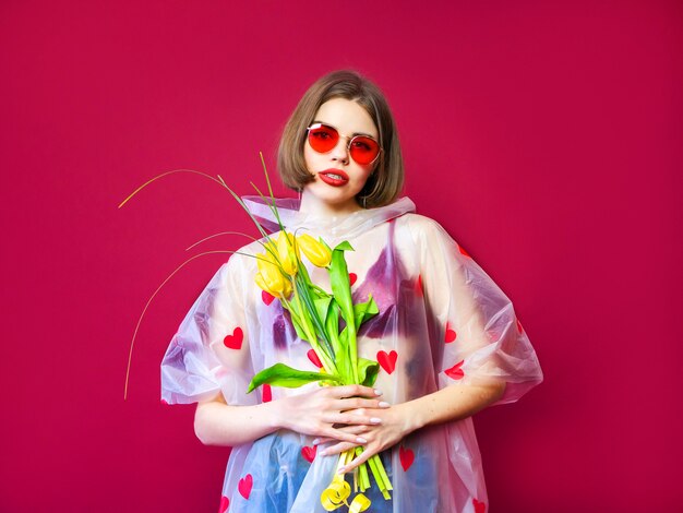 美容モデル春の花の束とレインコートの女。黄色いチューリップの花の花束を持つ美しい少女。幸せな驚きのモデルの女性が花の臭いがします。母の日ギフトバレンタイン・デー。