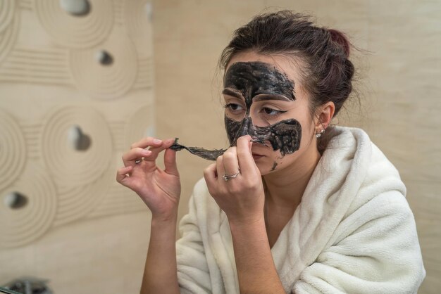 Beauty near the mirror removes a black mask film from black dots in the bathroom The concept of a black mask for acne