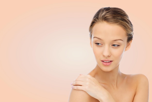 beauty, people, body care and health concept - smiling young woman face and hand on bare shoulder over beige background