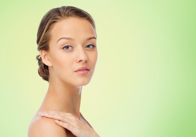 beauty, people, body care and health concept - smiling young woman face and hand on bare shoulder over green natural background