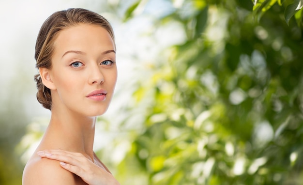 beauty, people, body care and health concept - smiling young woman face and hand on bare shoulder over green natural background