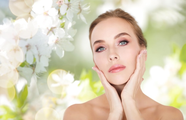 beauty, people and bodycare concept -beautiful young woman face and hands over natural spring cherry blossom background