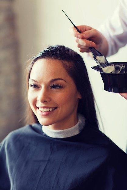 beauty and people concept - happy young woman with hairdresser coloring hair at salon