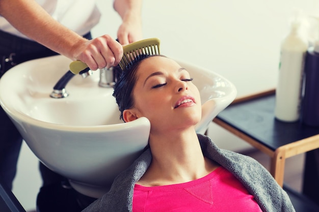 Foto concetto di bellezza e persone - giovane donna felice con il parrucchiere che pettina i capelli bagnati dopo il lavaggio al salone