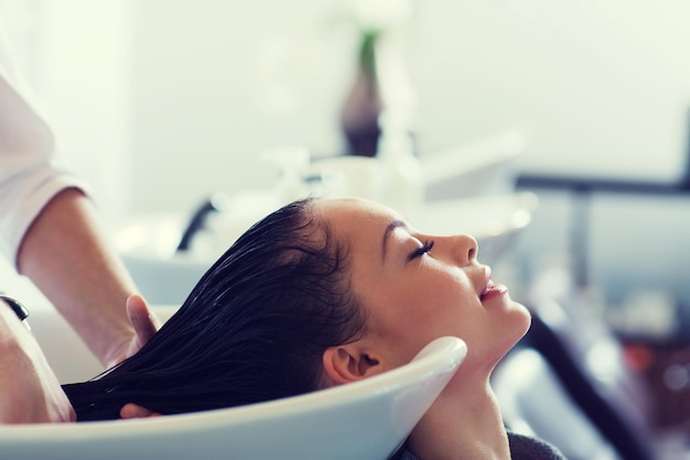 beauty and people concept - happy young woman with hairdresser washing head at hair salon