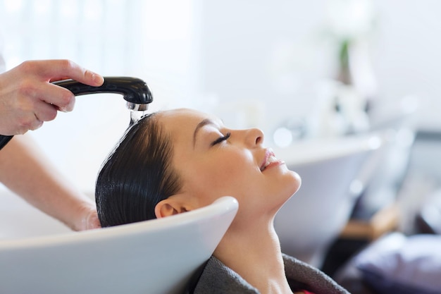 beauty and people concept - happy young woman with hairdresser washing head at hair salon