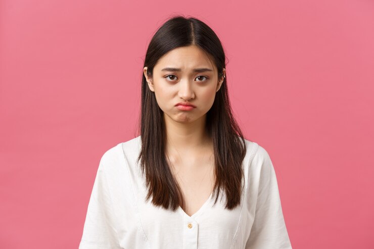 Photo 美しさ、人々の感情、夏のレジャーのコンセプト。白いドレスを着て、落ち込んで悲しい若いアジアの女性、ふくれっ面と眉をひそめている不本意な見ている動揺カメラ、立っているピンクの背景