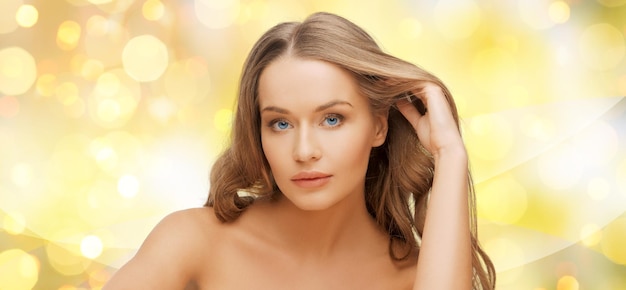 beauty, people, hair care, holidays and health concept - beautiful young woman face over yellow lights background