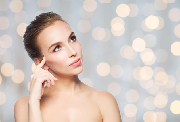 beauty, people and health concept - beautiful young woman looking up over holidays lights background