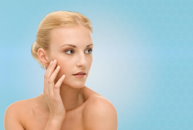 beauty, people and health concept - beautiful young woman touching her face over blue background