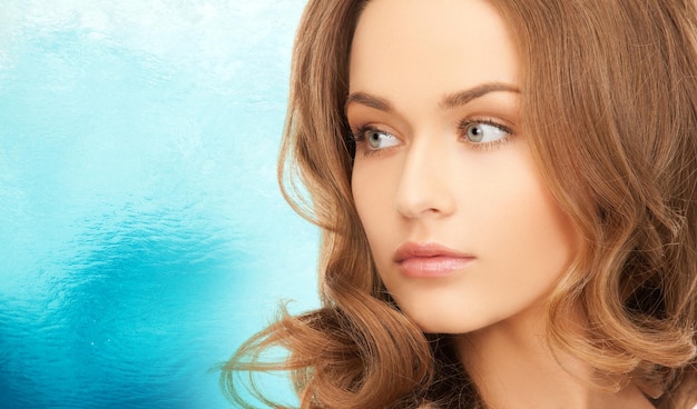 beauty, people and health concept - beautiful young woman with bare shoulders over blue ripple water background