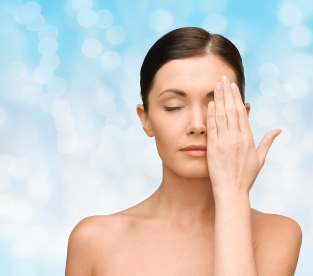 beauty, people and health concept - smiling young woman covering half of face with hand over blue lights background