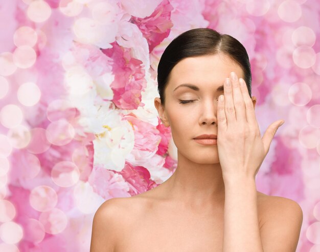 beauty, people and health concept - smiling young woman covering half of face with hand over pink lights background