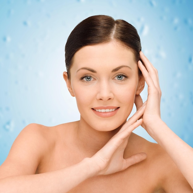 beauty, people and health concept - smiling young woman with bare shoulders over blue wet background