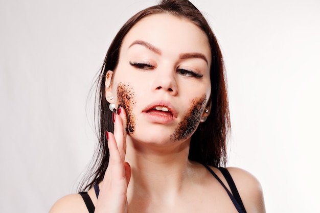 Beauty, people and healthy skin concept - Brunette cleanses skin coffee scrub white background Beauty Portrait. Beautiful Spa Woman Touching her Face. Perfect Fresh Skin Youth and Skin Care Concept