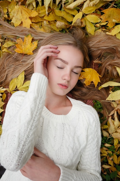 Beauty, people, season and health concept - pretty girl is lying in yellow Autumn leaves