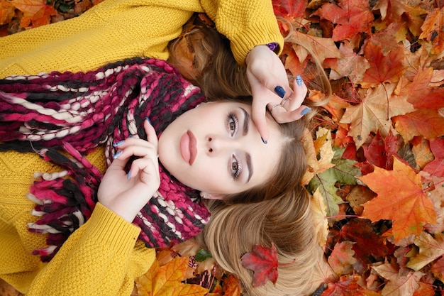 Beauty, people, season and health concept - pretty girl is lying in yellow red Autumn leaves