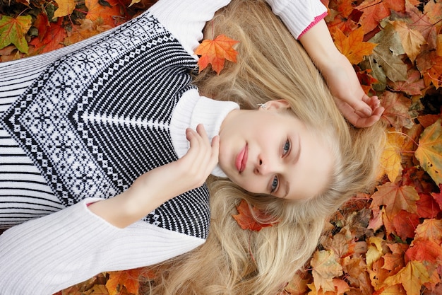 Beauty, people, season and health concept - pretty girl is lying in yellow red Autumn leaves