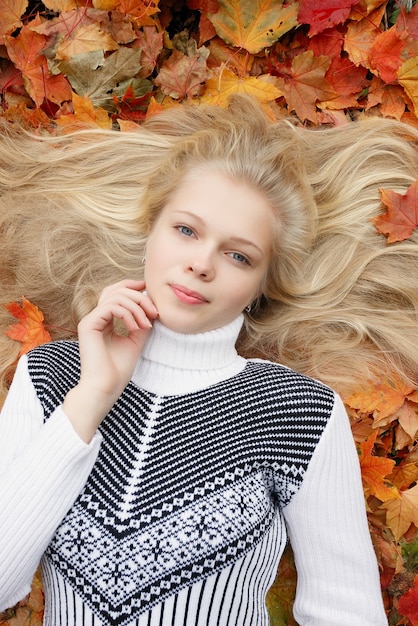 Beauty, people, season and health concept - pretty girl is lying in yellow red Autumn leaves