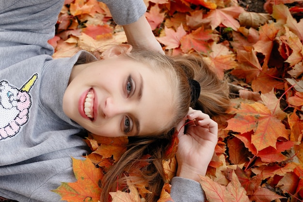 Beauty, people, season and health concept - pretty little girl is lying in yellow Autumn leaves