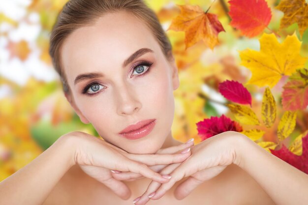 Photo beauty, people, season, season and bodycare concept -beautiful young woman face and hands over autumn leaves background