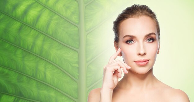 Photo beauty, people and skin care concept - beautiful young woman showing her cheekbone over natural green leaf background