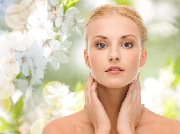 beauty, people, summer, spring and health concept - beautiful young woman touching her neck over green blooming garden background