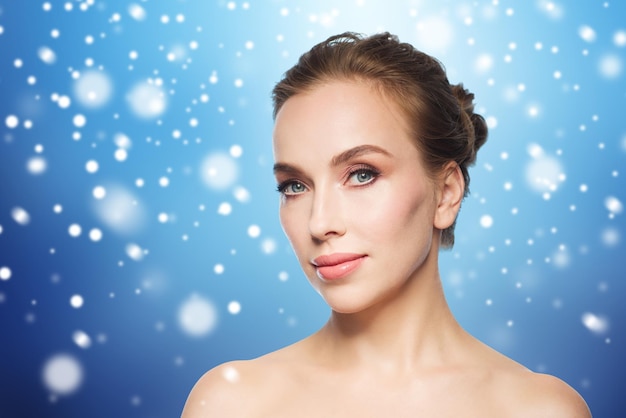 beauty, people, winter and health concept - beautiful young woman face over blue background and snow