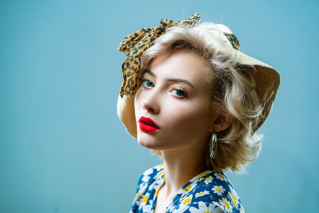 Beauty pin up girl on blue wall Young woman dressed in pinup style Blond model in retro hat posing o