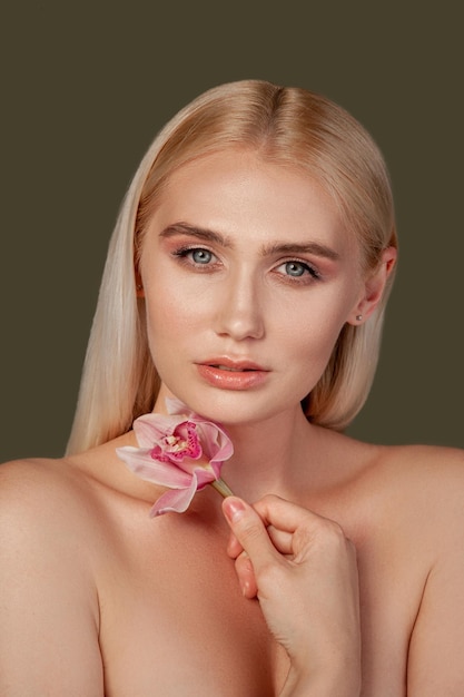 Beauty portrait Aesthetic cosmetology Blonde woman with bare shoulders holding orchid flower isolated on brown